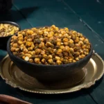 Geröstete Kichererbsen in einer dunkelblauen Schüssel, die auf einem Silbernen Teller steht. Im Hintergrund ein dunkelblau gestrichener Holztisch.