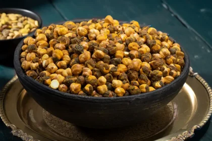 Geröstete Kichererbsen in einer dunkelblauen Schüssel, die auf einem Silbernen Teller steht. Im Hintergrund ein dunkelblau gestrichener Holztisch.