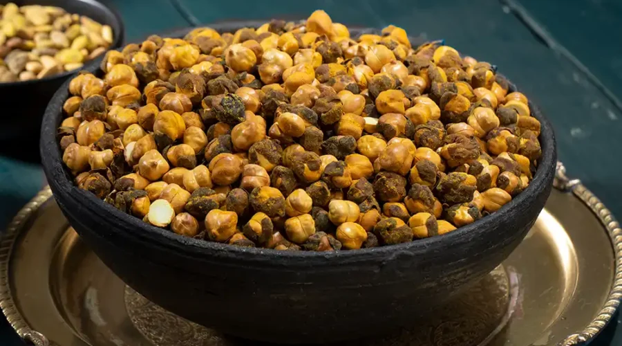 Geröstete Kichererbsen in einer dunkelblauen Schüssel, die auf einem Silbernen Teller steht. Im Hintergrund ein dunkelblau gestrichener Holztisch.