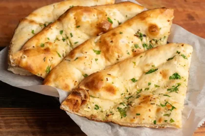 Auf einem Holztisch steht ein Teller, auf dem vier Stücke Naan-Brot aufgereiht sind. Das Brot ist mit kleingehackter Petersilie bestreut.