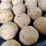 Viele noch ungekochte Semmelknödel liegen in Reihen nebeneinander auf einem Brett.