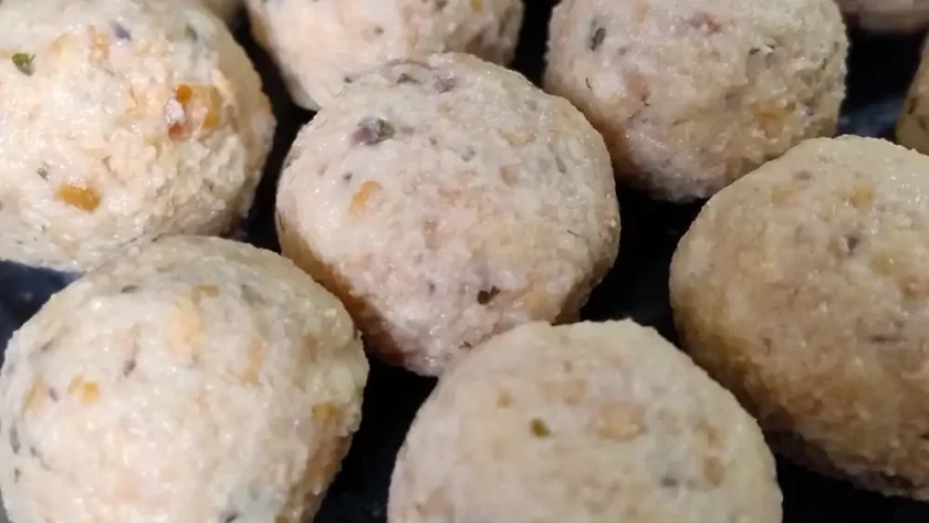 Viele noch ungekochte Semmelknödel liegen in Reihen nebeneinander auf einem Brett.