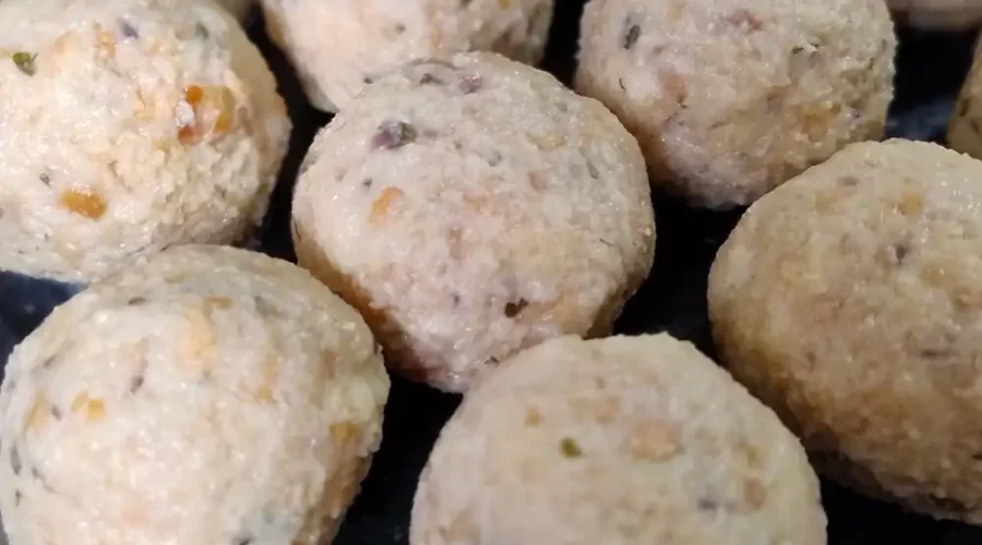 Viele noch ungekochte Semmelknödel liegen in Reihen nebeneinander auf einem Brett.