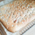 Ein frisch gebackenes Fladenbrot so groß wie ein Backblech liegt auf einem Gitter zum Auskühlen