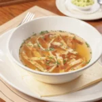 Weiße Schüssel gefüllt mit Brühe und fein geschnittenen Flädle