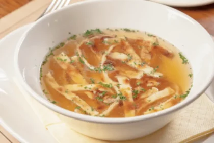 Weiße Schüssel gefüllt mit Brühe und fein geschnittenen Flädle