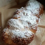 Ein mit viel Puderzucker bestreuter Hefezopf liegt auf eine zerknitterten Backpapier.