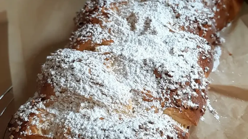 Ein mit viel Puderzucker bestreuter Hefezopf liegt auf eine zerknitterten Backpapier.
