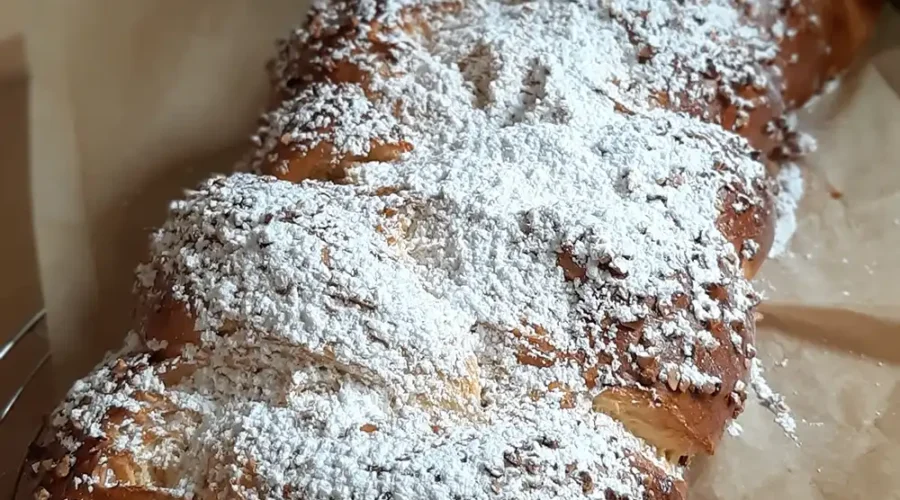 Ein mit viel Puderzucker bestreuter Hefezopf liegt auf eine zerknitterten Backpapier.