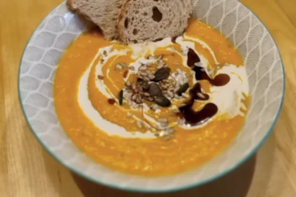 Kürbiscremesuppe in einer Schüssel garniert mit Sahne, Kürbiskernöl und Kürbiskernen, angerichtet mit einer Scheibe Brot
