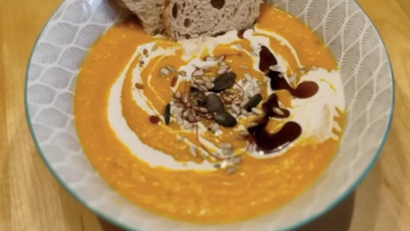 Kürbiscremesuppe in einer Schüssel garniert mit Sahne, Kürbiskernöl und Kürbiskernen, angerichtet mit einer Scheibe Brot