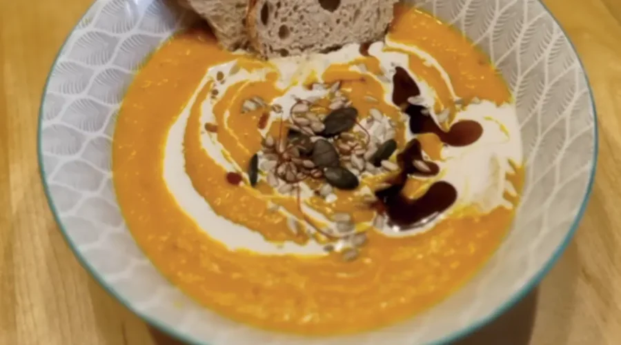 Kürbiscremesuppe in einer Schüssel garniert mit Sahne, Kürbiskernöl und Kürbiskernen, angerichtet mit einer Scheibe Brot