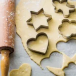 Ausgerollter Teig, aus dem Sterne und Herzen ausgestochen werden.