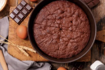 Schokoladen-Rührkuchen in einer runden Backform auf einem Holztisch, daneben liegen Eier und Schokolade