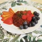 Schokoladenporridge auf einem Teller angerichtet mit frischen Beeren, garniert mit in feine Streifen geschnittener Minze