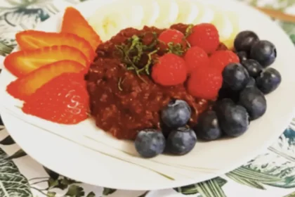 Schokoladenporridge auf einem Teller angerichtet mit frischen Beeren, garniert mit in feine Streifen geschnittener Minze