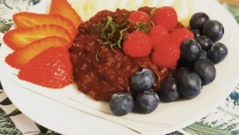 Schokoladenporridge auf einem Teller angerichtet mit frischen Beeren, garniert mit in feine Streifen geschnittener Minze