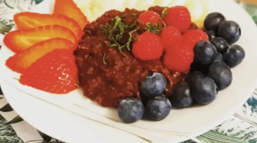 Schokoladenporridge auf einem Teller angerichtet mit frischen Beeren, garniert mit in feine Streifen geschnittener Minze