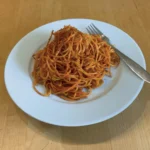 Tomatige Spaghetti auf einem weißen Teller mit Gabel