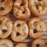 Mehrere kleine goldbraun gebackene Brezeln liegen nebeneinander auf einem Gitter zum Auskühlen.