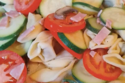 Nahaufnahme von einer Mischung aus Tortellini mit Zucchini- und Tomatenscheiben, Champignons und Kochschinken-Streifen.
