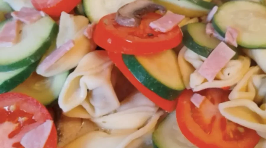 Nahaufnahme von einer Mischung aus Tortellini mit Zucchini- und Tomatenscheiben, Champignons und Kochschinken-Streifen.