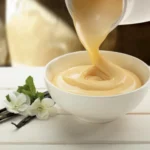 Vanillesoße wird aus einem Porzellankrug in eine kleine Schüssel gegossen.