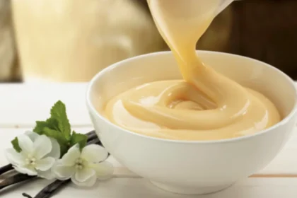 Vanillesoße wird aus einem Porzellankrug in eine kleine Schüssel gegossen.