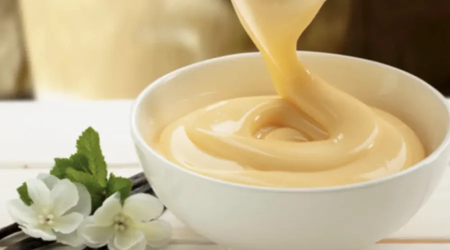 Vanillesoße wird aus einem Porzellankrug in eine kleine Schüssel gegossen.