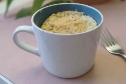 Eine große Tasse steht auf einem Tisch. Die Tasse ist gefüllt mit einem Kuchen, neben der TAsse liegt eine Gabel.