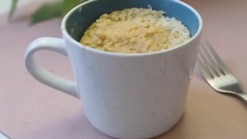 Eine große Tasse steht auf einem Tisch. Die Tasse ist gefüllt mit einem Kuchen, neben der TAsse liegt eine Gabel.