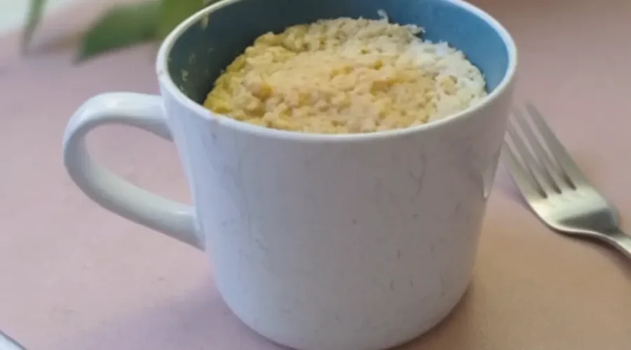 Eine große Tasse steht auf einem Tisch. Die Tasse ist gefüllt mit einem Kuchen, neben der TAsse liegt eine Gabel.