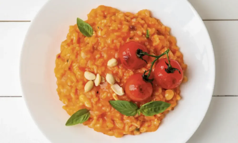 Von oben fotografierter weißer Porzellanteller gefüllt mit tomatigem Risotto, garniert mit gerösteten Rispen-Tomaten.
