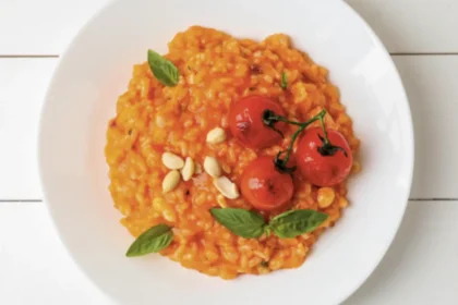 Von oben fotografierter weißer Porzellanteller gefüllt mit tomatigem Risotto, garniert mit gerösteten Rispen-Tomaten.