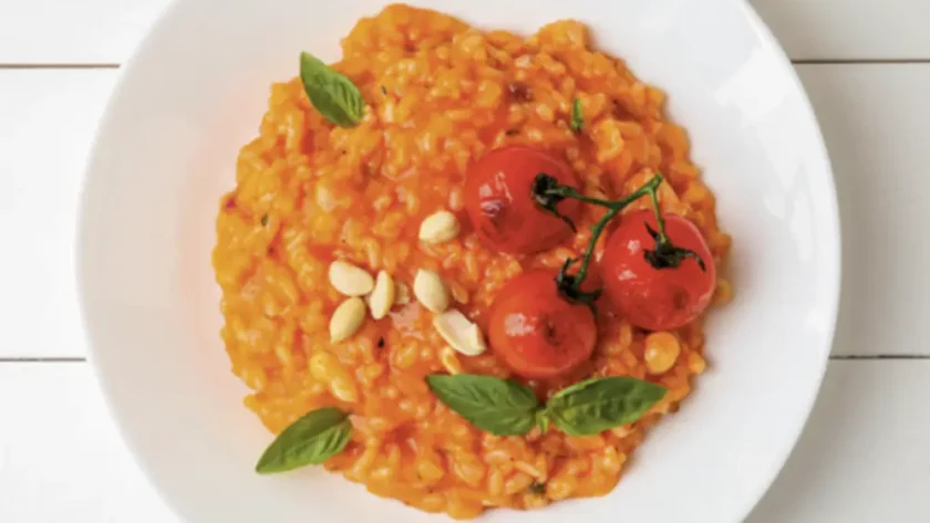 Von oben fotografierter weißer Porzellanteller gefüllt mit tomatigem Risotto, garniert mit gerösteten Rispen-Tomaten.