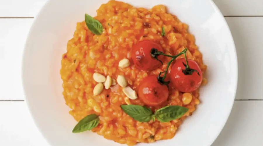 Von oben fotografierter weißer Porzellanteller gefüllt mit tomatigem Risotto, garniert mit gerösteten Rispen-Tomaten.